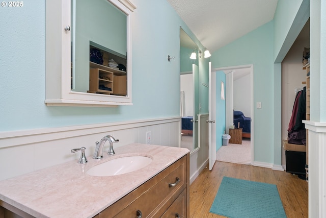 bathroom with a wainscoted wall, vanity, wood finished floors, and lofted ceiling