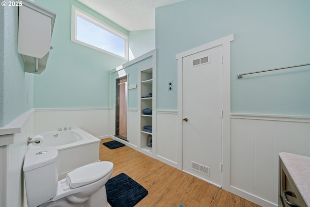 full bathroom featuring wainscoting, toilet, a bath, and visible vents