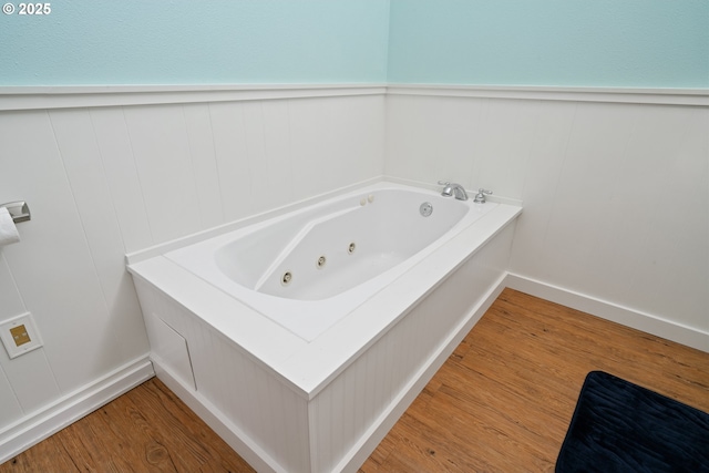 bathroom featuring a wainscoted wall, a decorative wall, a tub with jets, and wood finished floors