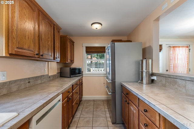 11005 SW 35th Ave, Portland, OR 97219 - kitchen with appliances with stainless steel finishes, tile counters, brown cabinetry, and light tile patterned flooring