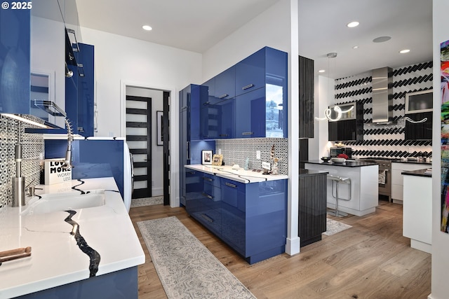 kitchen featuring blue cabinetry, sink, decorative light fixtures, light hardwood / wood-style floors, and wall chimney range hood