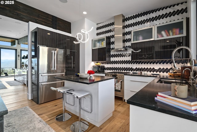 kitchen featuring a kitchen island, sink, a breakfast bar area, stainless steel appliances, and wall chimney range hood