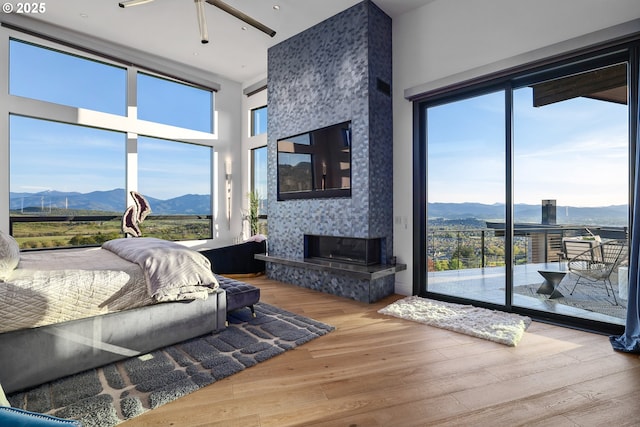 bedroom with access to exterior, a mountain view, a fireplace, hardwood / wood-style floors, and a high ceiling