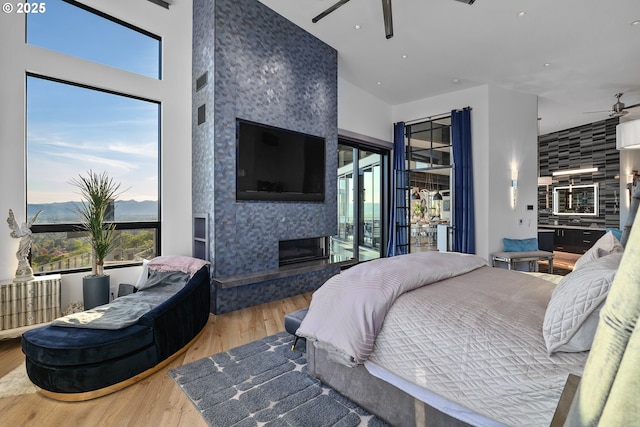 bedroom featuring access to exterior, a fireplace, wood-type flooring, and a high ceiling