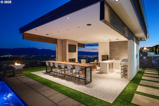 patio terrace at dusk featuring an outdoor kitchen, an outdoor fire pit, exterior bar, and a mountain view