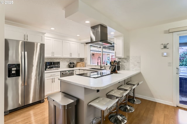 kitchen with a breakfast bar, range hood, a sink, light wood finished floors, and appliances with stainless steel finishes