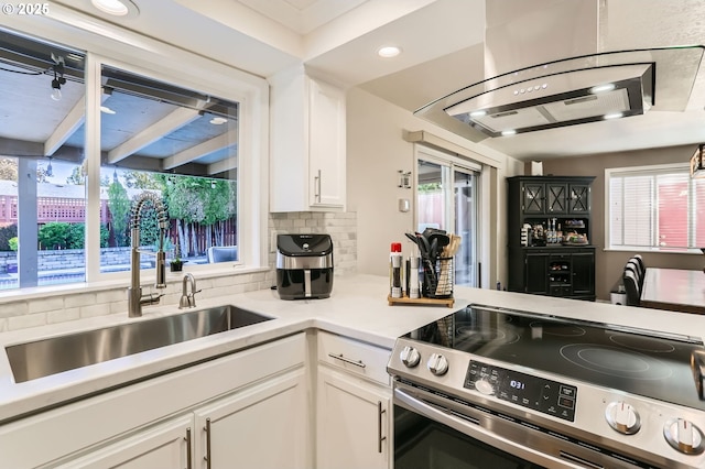 kitchen with a sink, decorative backsplash, white cabinetry, and stainless steel range with electric stovetop