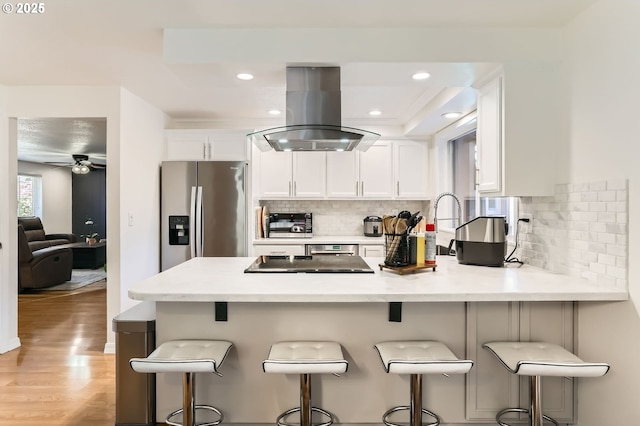 kitchen featuring island range hood, light countertops, a peninsula, stainless steel fridge, and white cabinetry