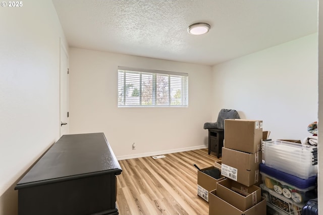 office area featuring baseboards, light wood-type flooring, and a textured ceiling
