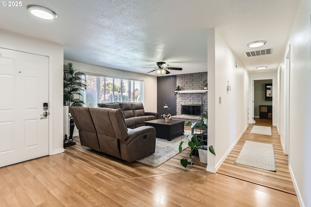 living room featuring a fireplace, light wood-style floors, a textured ceiling, a ceiling fan, and visible vents