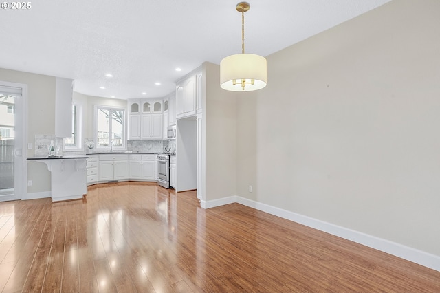 kitchen featuring appliances with stainless steel finishes, decorative light fixtures, white cabinetry, backsplash, and light hardwood / wood-style floors