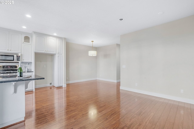 kitchen with a breakfast bar, white cabinetry, light hardwood / wood-style flooring, appliances with stainless steel finishes, and pendant lighting