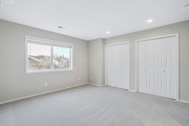 unfurnished bedroom featuring multiple closets and light colored carpet