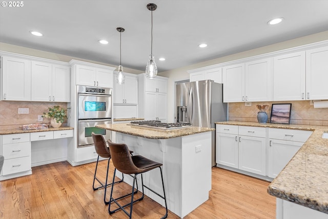 kitchen with white cabinets, light wood finished floors, appliances with stainless steel finishes, and a kitchen island