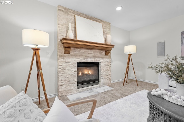 living area featuring baseboards, a stone fireplace, and carpet flooring