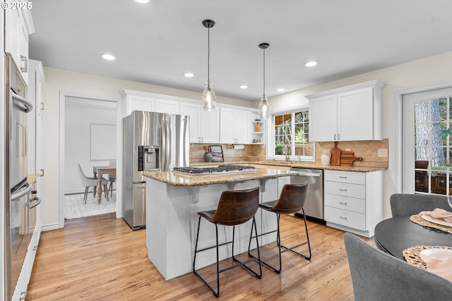 kitchen featuring light wood finished floors, a breakfast bar, light stone counters, white cabinets, and stainless steel appliances