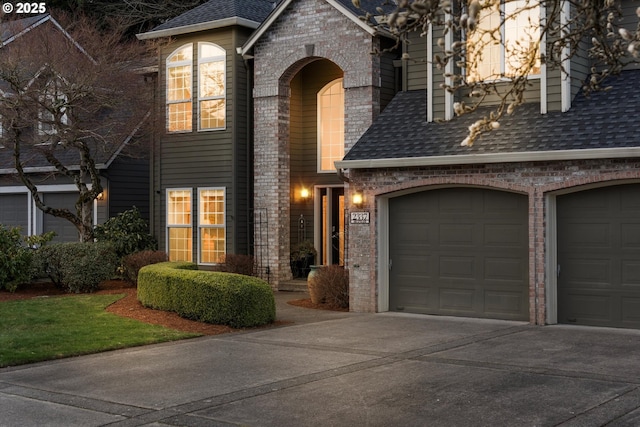 view of front of home featuring brick siding, driveway, an attached garage, and roof with shingles