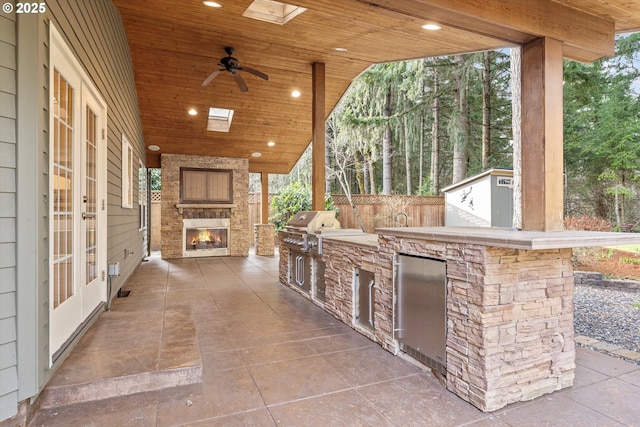 view of patio with fence, grilling area, french doors, an outdoor stone fireplace, and an outdoor kitchen