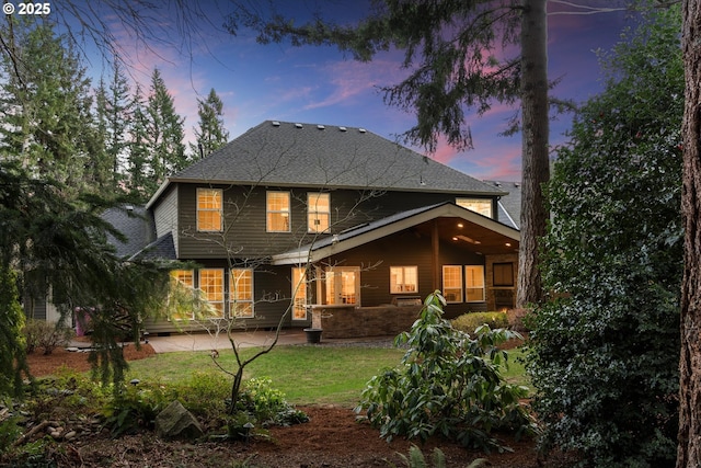 back of house featuring a patio area, a lawn, and roof with shingles