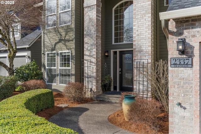 doorway to property featuring brick siding and a shingled roof