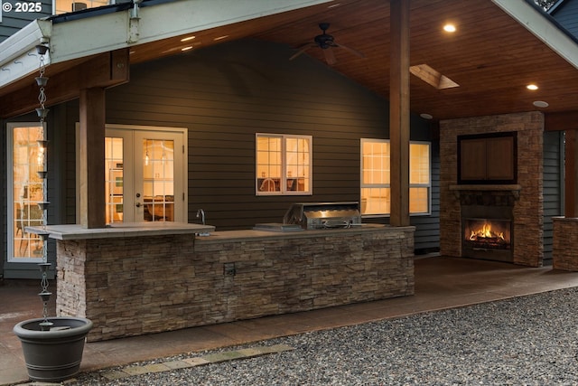 view of patio / terrace with french doors, a lit fireplace, area for grilling, and a ceiling fan