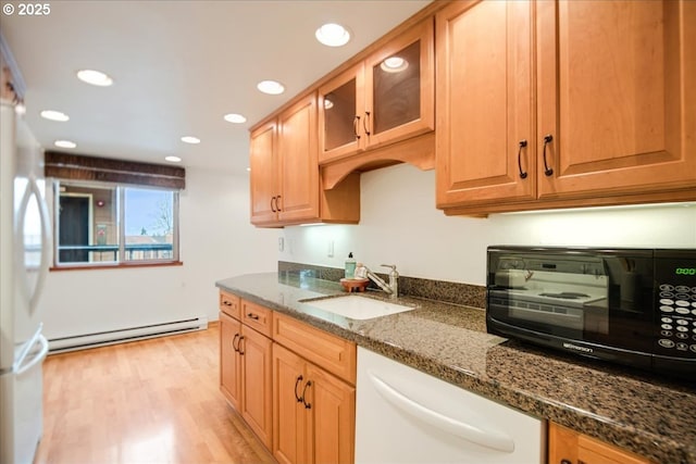 kitchen featuring dark stone counters, baseboard heating, light wood-style floors, white appliances, and a sink