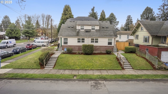 view of front facade with brick siding, fence, stairway, roof with shingles, and a front yard