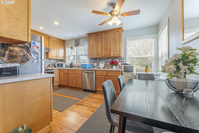 kitchen with white microwave, light wood-style flooring, light countertops, dishwasher, and backsplash