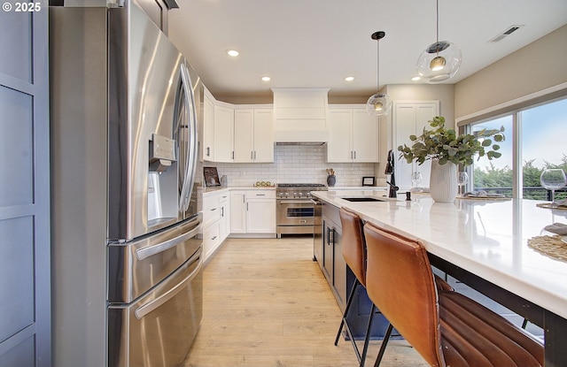 kitchen with sink, appliances with stainless steel finishes, hanging light fixtures, white cabinets, and custom exhaust hood