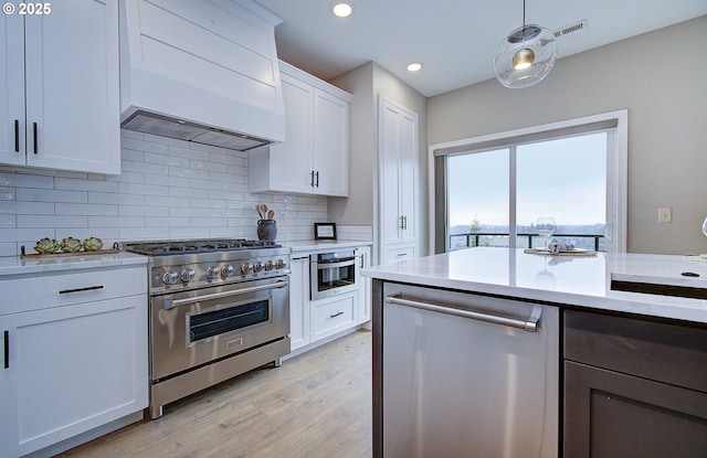 kitchen with custom exhaust hood, decorative light fixtures, light hardwood / wood-style flooring, appliances with stainless steel finishes, and white cabinets