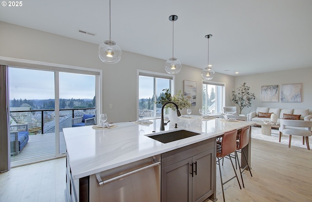 kitchen with sink, a center island with sink, decorative light fixtures, stainless steel dishwasher, and light wood-type flooring