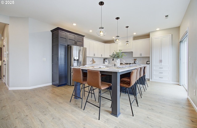 kitchen with stainless steel refrigerator with ice dispenser, decorative light fixtures, a kitchen breakfast bar, and light hardwood / wood-style flooring