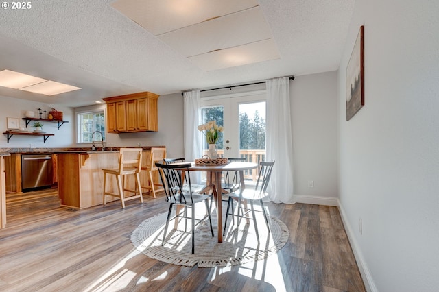 dining area with sink, a textured ceiling, light wood-type flooring, and french doors