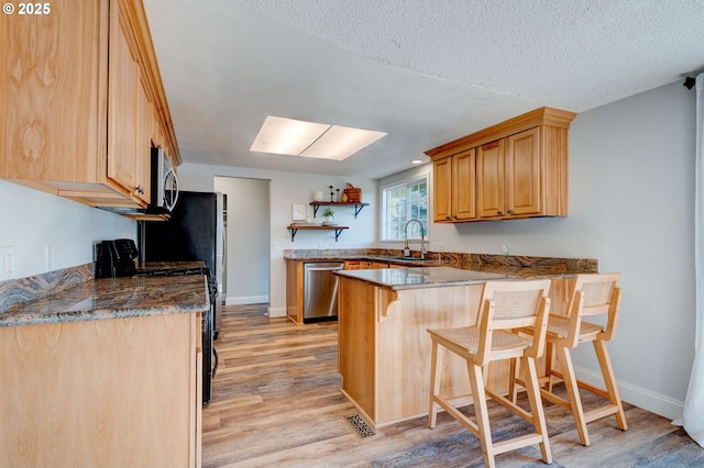 kitchen with appliances with stainless steel finishes, sink, a breakfast bar area, kitchen peninsula, and light wood-type flooring