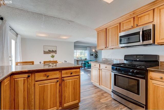 kitchen featuring stainless steel appliances, light hardwood / wood-style floors, a textured ceiling, and light brown cabinets