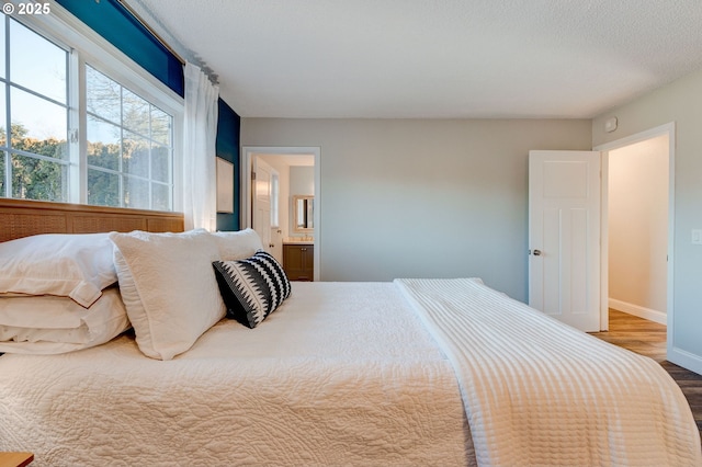 bedroom featuring wood-type flooring, a textured ceiling, and ensuite bath