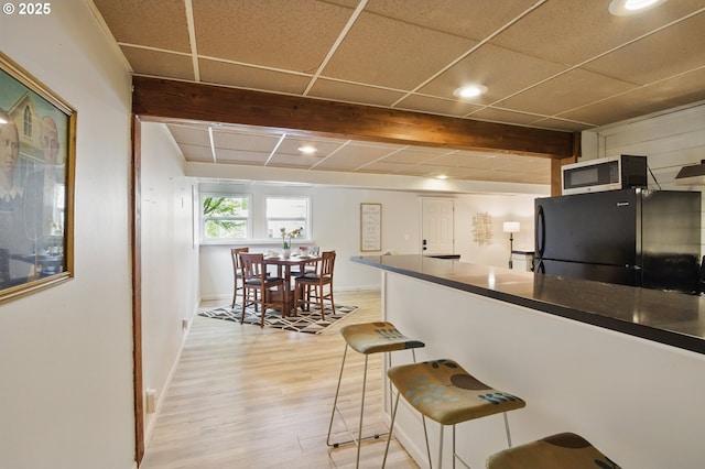 kitchen featuring beam ceiling, dark countertops, freestanding refrigerator, recessed lighting, and light wood-style floors
