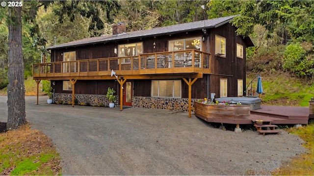 view of front of house featuring a deck, metal roof, a standing seam roof, a chimney, and a hot tub