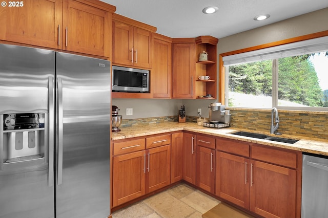 kitchen with stainless steel appliances, a sink, brown cabinetry, light stone counters, and recessed lighting