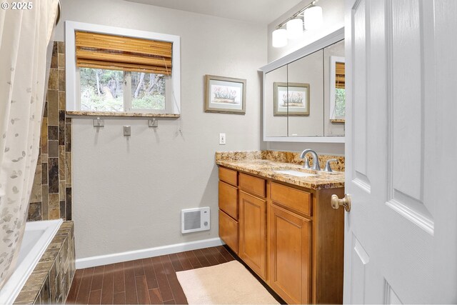 bathroom with baseboards, wood finished floors, vanity, and tiled shower / bath