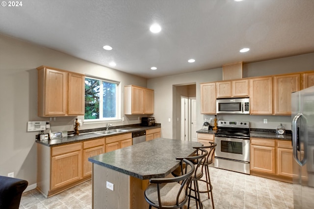 kitchen with light brown cabinetry, sink, stainless steel appliances, and a center island