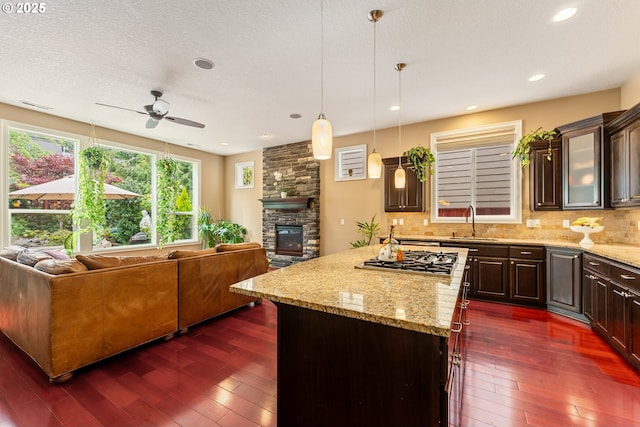 3356 NW 153rd Ter, Portland, OR 97229 - kitchen with open floor plan, stainless steel gas cooktop, a stone fireplace, ceiling fan, and a textured ceiling