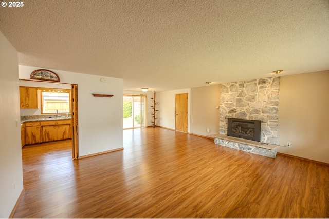 745 N 8th St, Lakeside, OR 97449 - unfurnished living room with a textured ceiling, a sink, wood finished floors, a fireplace, and baseboards