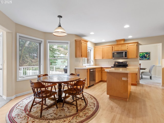 kitchen with light wood-style flooring, stainless steel appliances, a sink, light countertops, and a center island