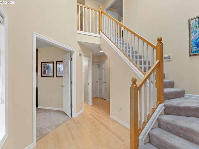 stairway featuring a towering ceiling, baseboards, and wood finished floors