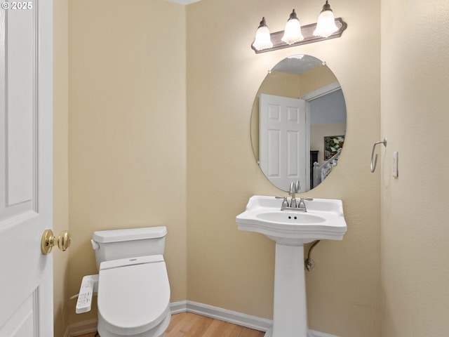 half bathroom featuring baseboards, a sink, toilet, and wood finished floors