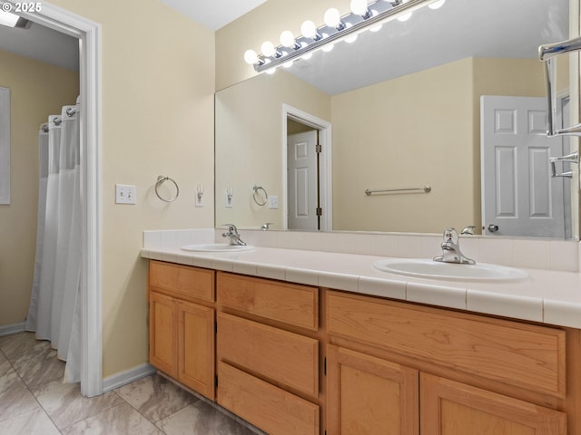 full bathroom featuring double vanity, marble finish floor, baseboards, and a sink