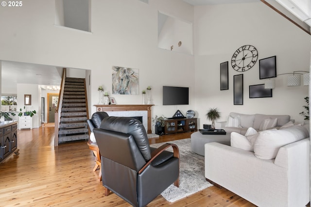 living room featuring light wood-style floors, high vaulted ceiling, a fireplace with raised hearth, and stairs
