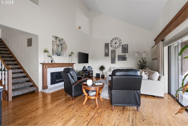 living area featuring visible vents, a fireplace, light wood-style floors, high vaulted ceiling, and stairway