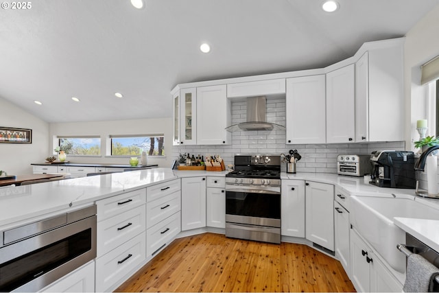 kitchen with wall chimney range hood, appliances with stainless steel finishes, white cabinetry, recessed lighting, and decorative backsplash